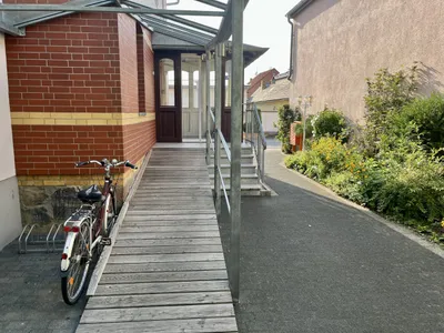 Überdachte Rampe mit Handlauf, die stufenlos zum Eingang führt; daneben stehen Fahrräder.
