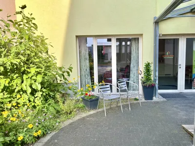 Terrasse vor dem Eingang mit Tisch und Stühlen, eingerahmt von Kübelpflanzen.