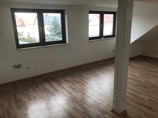 Wohnraum im Dachgeschoss mit Dachschräge, zwei Gaubenfenstern und einer weiß gestrichenen Stütze.